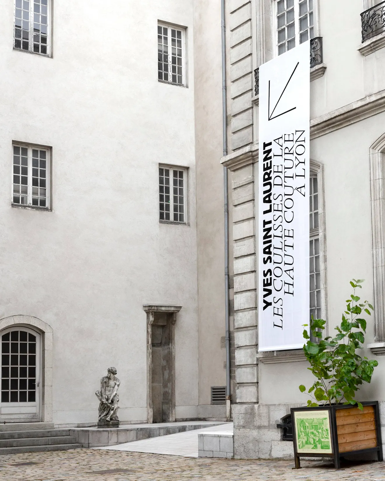 Bannière verticale signalétique d'exposition Yves Saint Laurent sur la façade du Musée des Tissus de Lyon — design print pour communication d'exposition muséale, graphiste freelance Occitanie
